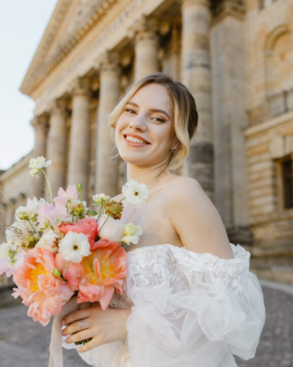 Lächelnde Braut mit Blumen vor klassischer Architektur