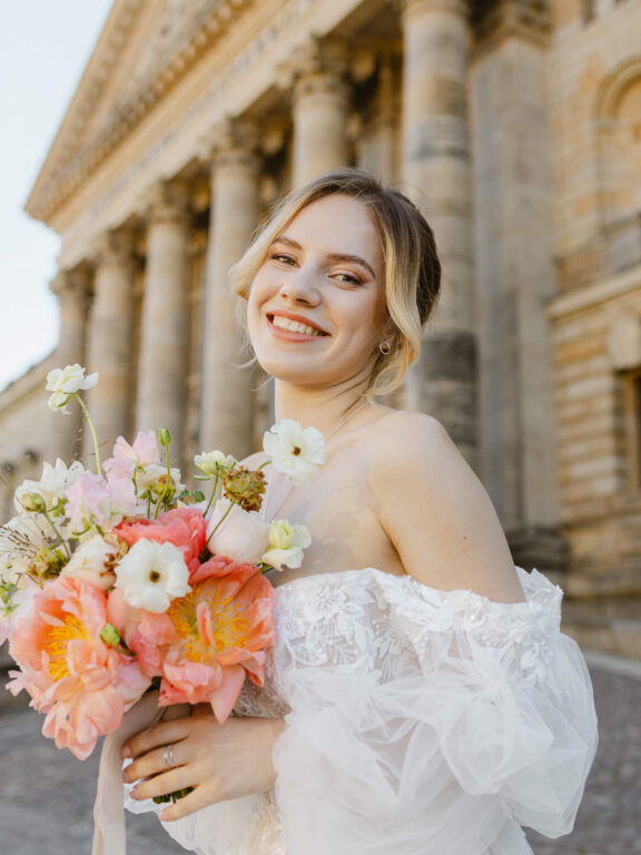 Lächelnde Braut mit Blumen vor klassischer Architektur